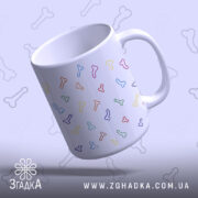 Чашка з кольоровими піструнами, біла з малюнками кісточок різних кольорів, зображена під кутом, фон світло-фіолетовий, ручка стандартна, край рівний, глянцева поверхня.