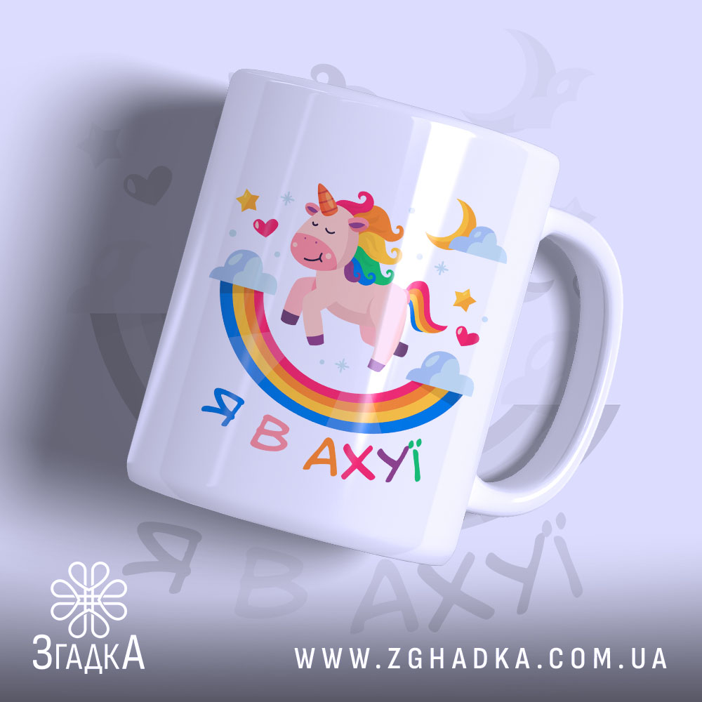 Чашка зі здивованим єдинорогом, білого кольору, з ракурсу спереду, на фоні світло-фіолетового кольору. Принт містить єдинорога, веселку, зірки та напис 'Я В АХУЙ'. Ручка чашки гладка, край рівний, поверхня глянцева.