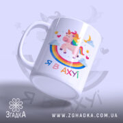 Чашка зі здивованим єдинорогом, білого кольору, з ракурсу знизу, на фоні світло-фіолетового кольору. Принт містить єдинорога, веселку, зірки та напис 'Я В АХУЙ'. Ручка чашки гладка, край рівний, поверхня глянцева.