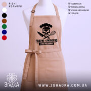 Фартух годую з любов’ю, бежевого кольору, зображений на манекені з нейтральним фоном, принт з черепом та кухонними приладами розташований по центру.