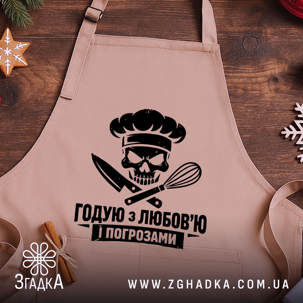 Фартух годую з любов’ю, бежевого кольору, зображений на дерев'яному фоні з елементами декору, принт з черепом та кухонними приладами розташований по центру.