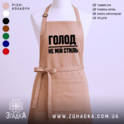Фартух голод не мій стиль. Фартух бежевого кольору, зображений з фронтального ракурсу на манекені. Фон світлий, без зайвих деталей. Принт чорного кольору з написом 'ГОЛОД НЕ МІЙ СТИЛЬ'.