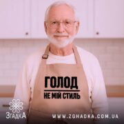 Фартух голод не мій стиль. Бежевий фартух, знятий зверху на дерев'яному фоні. На фоні присутні декорації у вигляді новорічних елементів. Принт чорного кольору з написом 'ГОЛОД НЕ МІЙ СТИЛЬ'.