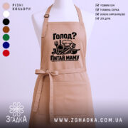 Фартух голод питай маму. Фартух бежевого кольору, зображений з фронтального ракурсу на манекені. Фон світлий, з елементами тексту та символікою на фартусі, що включає кухонні прилади.
