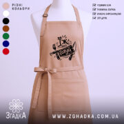 Фартух їж або готуй, бежевого кольору, зображений з ракурсу спереду на манекені, фон світлий, принт чорного кольору з написом 'Їж або готуй' та зображенням виделки і ножа.