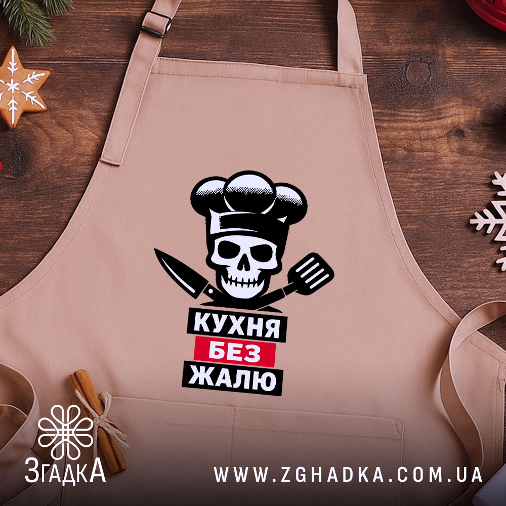 Фартух кухня без жалю, бежевого кольору, зображений на дерев'яному фоні, принт з черепом, кухарським ковпаком та кухонними приладдями, декорований новорічними елементами.