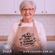 Фартух менше слів більше смаку. Бежевий фартух з чорним принтом, зображений на манекені, фон світлий, деталі принта включають кухонні атрибути, такі як каструля і спеції.