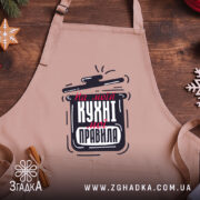 Фартух моя кухня правила. Фартух бежевого кольору, зображений з верхнього ракурсу, фон дерев'яний, принт з написом "На моїй кухні мої правила" в чорному та червоному кольорах, поруч декор у вигляді новорічних зірочок та печива.