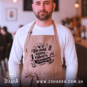 Фартух на моїй кухні, бежевого кольору, з фронтального ракурсу, на чоловікові з бородою, фон затишного кафе, принт з написом 'На моїй кухні худнуть тільки нерви' в чорному кольорі.