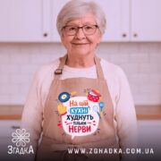 Фартух на цій кухні бежевого кольору, зображений з фронтального ракурсу на манекені, фон світлий, принт містить текст "На цій кухні худнуть тільки нерви" з ілюстраціями кухонного приладдя.