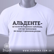 Футболка альденте стан життя. Біла футболка, складена на столі, з коротким рукавом. На фоні світло-сірого кольору, з чорним принтом, текст розташований по центру. На футболці є етикетка з зеленим шнурком.