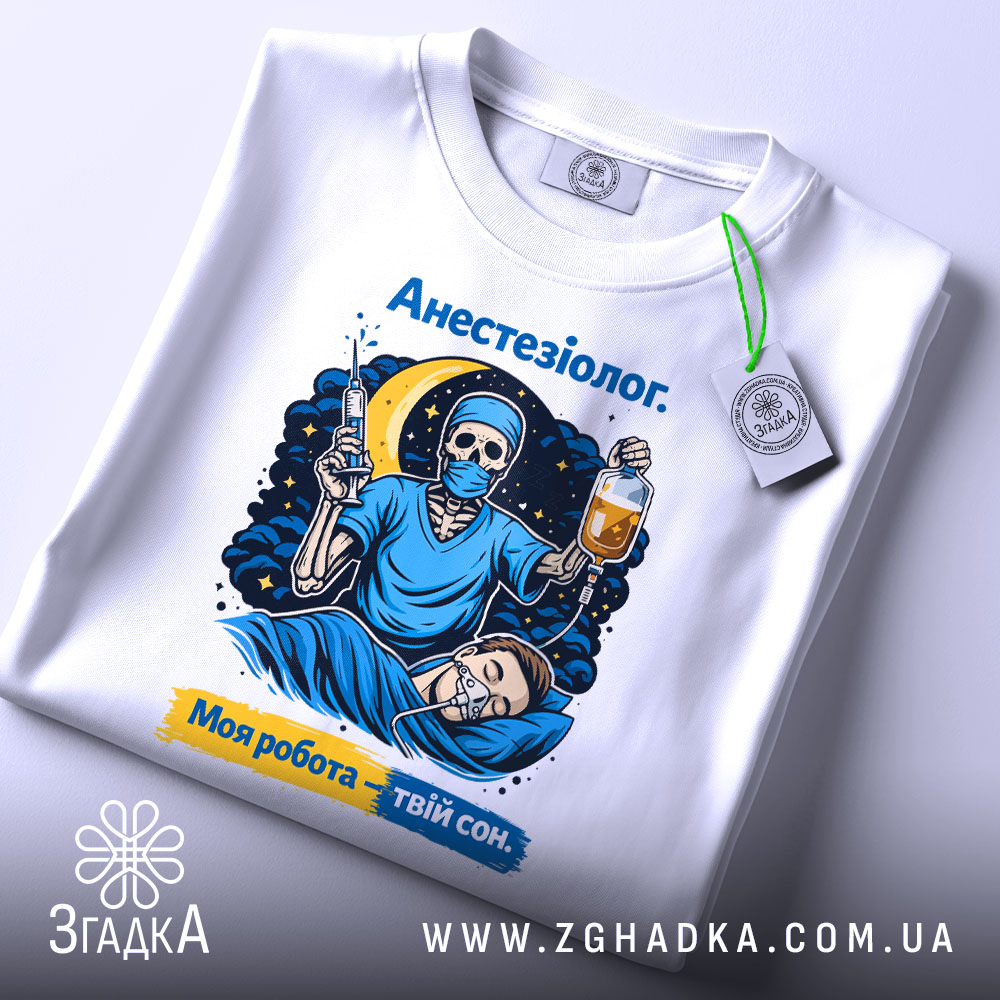 Футболка анестезіолог, біла, зображена зверху, фон світло-сірий, принт з черепом в масці, який тримає шприц і крапельницю, на фоні місяць і зірки, текст "Анестезіолог. Моя робота – твій сон.", з біркою на рукаві.