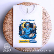 Футболка анестезіолог, біла, зображена зверху на плетеній кошику, фон світло-сірий, принт з черепом в масці, який тримає шприц і крапельницю, на фоні місяць і зірки, текст "Анестезіолог. Моя робота – твій сон."
