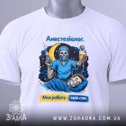 Футболка анестезіолог, біла, зображена зверху, фон світло-сірий, принт з черепом в масці, який тримає шприц і крапельницю, на фоні місяць і зірки, текст "Анестезіолог. Моя робота – твій сон.", з біркою на рукаві.