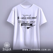 Футболка ангел на мітлі, біла, підвішена на вішалці, фон світло-сірий, принт чорного кольору з написом 'Я - ангел, чесне слово! Просто на мітлі ШВИДШЕ.' і малюнком мітли.