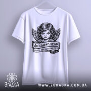 Футболка ангельське личко, біла, підвішена на вішалці, фон світло-сірий, принт з зображенням ангела з крилами та написом на стрічці.