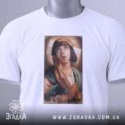 Футболка арт іронія віри, біла футболка, складена на столі, з принтом дівчини з молитвою, фон світло-сірий, на футболці є етикетка з зеленим шнурком.