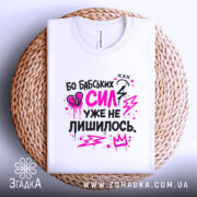 Футболка бабських сил. Біла футболка, складена на плетеній основі, з принтом у чорному та рожевому кольорах. На фоні видно текстуру плетення, що додає естетики.