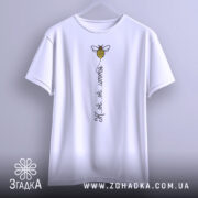 Футболка бджілка це життя. Біла футболка, підвішена на вішалці, з принтом бджілки та написом 'Ж.ж.ж.ж.'. Фон світлий, з легким градієнтом, що створює елегантний вигляд.