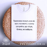 Футболка біль художника, біла, зображена на плетеній тарілці, фон світло-сірий, принт чорного кольору з текстом про художників.