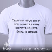 Футболка біль художника, біла, зображена зверху, на столі, фон світло-сірий, принт чорного кольору з текстом про художників, з зеленим ярликом.