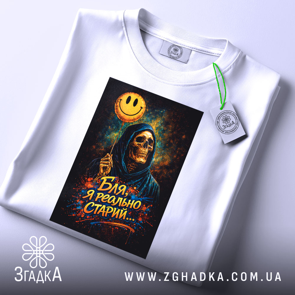 Футболка бля я старий, біла, зображена зверху, фон світлий, принт з черепом у капюшоні, що тримає жовту усміхнену кульку, на футболці є етикетка з зеленим шнурком.