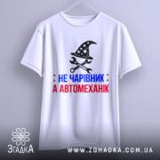 Футболка чарівник автомеханік, біла, підвішена на вішалці, фон світло-сірий, принт з магічним капелюхом та інструментами, текст червоний і синій.