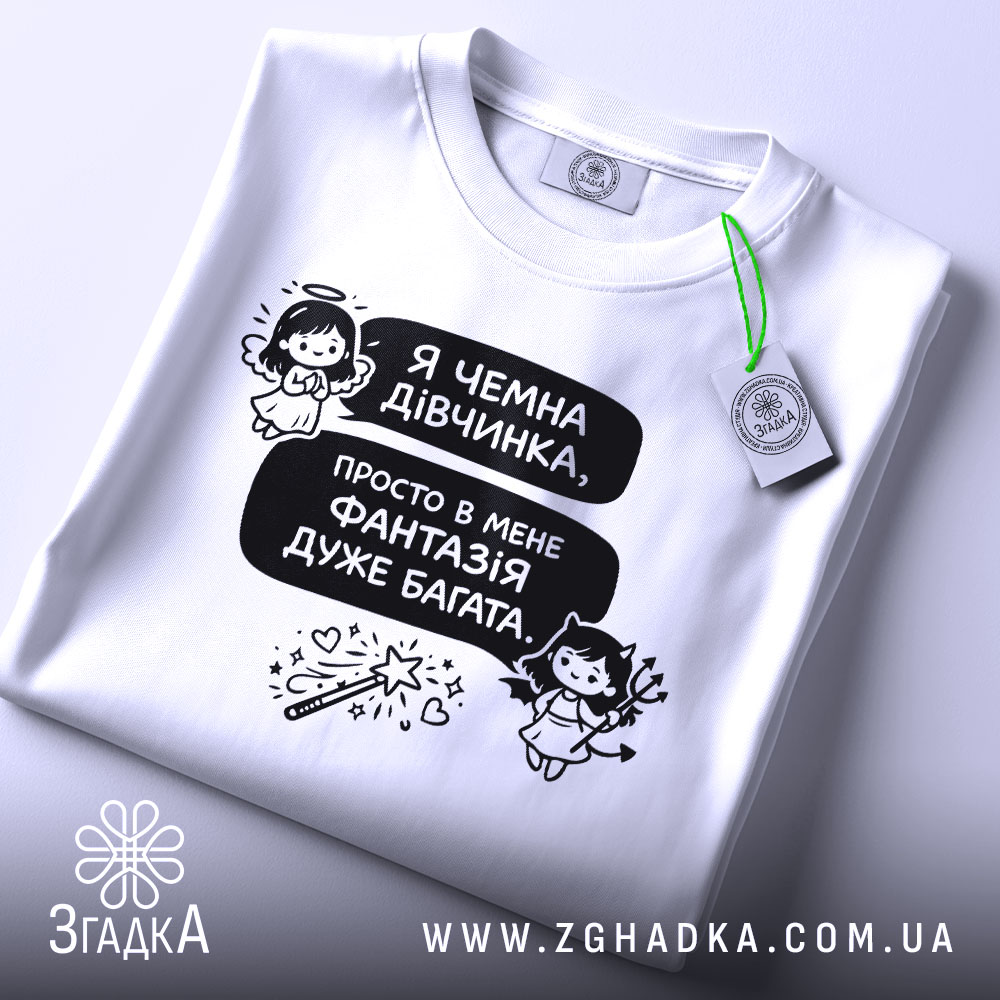Футболка чемна дівчинка, білого кольору, зображена зверху, на фоні світлого кольору, принт з текстом і малюнками ангела та дівчинки з чортом, з зеленим ярликом.