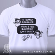 Футболка чемна дівчинка, білого кольору, зображена зверху, на фоні світлого кольору, принт з текстом і малюнками ангела та дівчинки з чортом, з зеленим ярликом.