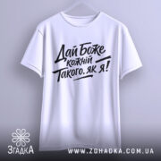 Футболка дай Боже кожному, біла, підвішена на вішалці, фон світло-сірий, принт чорного кольору з текстом 'Дай Боже кожний Такого, як я!' у стилі рукописного шрифту.