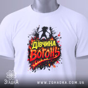 Футболка дівчина вогонь, біла, зображена зверху на столі, фон світлий, принт з написом 'Дівчина Вогонь' в червоних і жовтих кольорах, оточений вогняними ефектами, з зеленим ярликом.