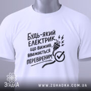 Футболка для електрика, білого кольору, складена на поверхні, фон світло-сірий, принт чорного кольору з текстом і малюнком електричної вилки, на футболці є етикетка.