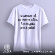 Футболка для тих хто працює. Біла футболка з чорним принтом, підвішена на вішалці. Фон світло-сірий, текст на футболці читається чітко: 'Не лається той, хто нічого не робить. А я піздець весь в роботі.'