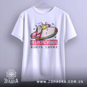 Футболка домашня королева, біла, підвішена на вішалці, фон світло-сірий, принт з малюнком домашніх капців і корони, текст "НАЙКРАСИВІША НАВІТЬ УДОМА" червоним кольором.