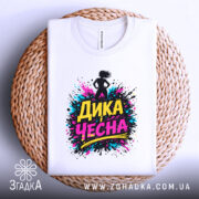 Футболка дика чесна, біла, складена на плоскій поверхні з плетеного матеріалу, фон світлий, принт з написом 'ДИКА ЧЕСНА' в яскравих кольорах.