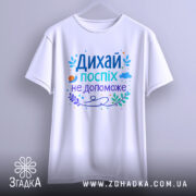 Футболка дихай спокійно, біла, зображена з фронтального ракурсу, фон нейтральний, принт з текстом "Дихай, поспіх не допоможе" в різних кольорах, з елементами рослинності та малюнком равлика.