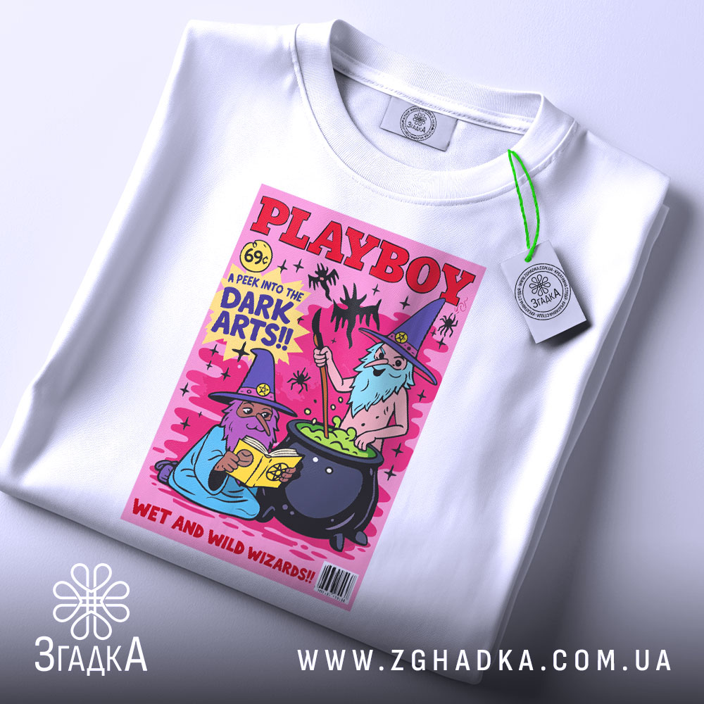 Футболка дикі чарівники, біла, зображена зверху, на ній є етикетка з зеленим шнурком, фон світлий, принт з двома чарівниками, один читає книгу, інший варить зілля, яскраві кольори на рожевому фоні.