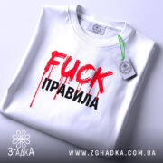Футболка fuck правила, біла, складена на поверхні, фон світло-сірий, принт червоний з краплями фарби та чорний текст, з етикеткою на комірці.