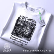 Футболка гетьмани змінюються. Біла футболка з чорним принтом, зображення гетьмана на фоні замку, ракурс зверху, видно етикетку з зеленим шнурком, принт чітко виділяється на фоні.