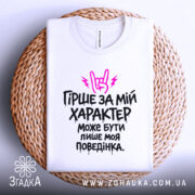 Футболка гірше ніж характер. Біла футболка, складена на плетеному кошику, з принтом чорного кольору та рожевими елементами. На фоні світло-сірого кольору, текст добре видно.