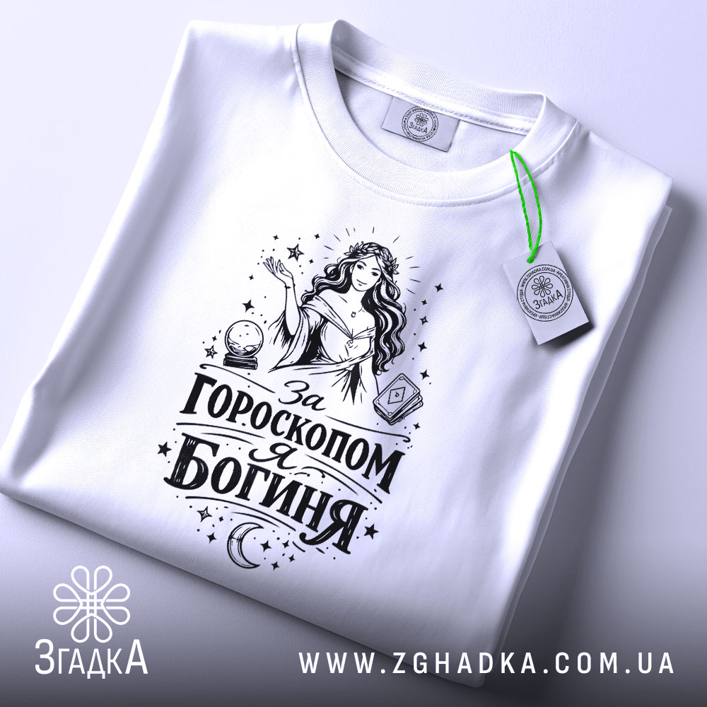 Футболка я богиня, біла, складена на поверхні, з видимим етикеткою, фон світло-сірий, принт чорного кольору з жінкою та астрологічними елементами.