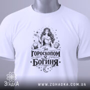 Футболка я богиня, біла, складена на поверхні, з видимим етикеткою, фон світло-сірий, принт чорного кольору з жінкою та астрологічними елементами.