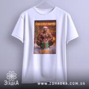 Футболка я маю подарунок, біла, з ракурсу спереду, на фоні світло-сірого кольору, принт з зображенням чоловіка в червоній шапці Санти, який сидить на снігу з подарунком.