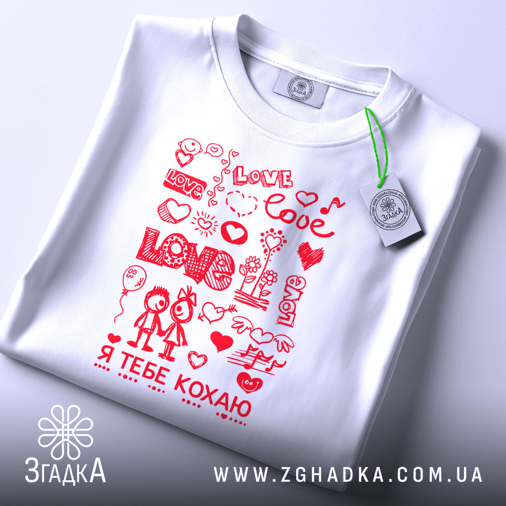 Футболка я тебе кохаю, біла, складена на поверхні, фон світло-сірий, принт червоний з малюнками сердець, квітів та двох персонажів, які тримаються за руки, на комірці є етикетка.