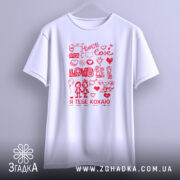 Футболка я тебе кохаю, біла, підвішена на вішалці, фон світло-сірий, принт червоний з малюнками сердець, квітів та двох персонажів, які тримаються за руки.