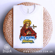 Футболка я в нормі майже білого кольору, складена на плетеній кошику, фон світло-сірий, принт з червоно-золотистою жінкою з мечем та написом "Я в нормі! Майже" у яскравих кольорах.