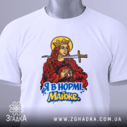Футболка я в нормі майже білого кольору, складена на поверхні, фон світло-сірий, принт з червоно-золотистою жінкою з мечем та написом "Я в нормі! Майже" у яскравих кольорах, з зеленим ярликом.