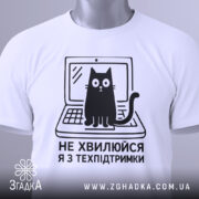 Футболка я з техпідтримки, білого кольору, зображена з верхнього ракурсу, на фоні світло-сірого кольору, принт чорного кольору з котом на ноутбуці та текстом 'НЕ ХВИЛЮЙСЯ Я З ТЕХПІДТРИМКИ', з етикеткою зеленого кольору.