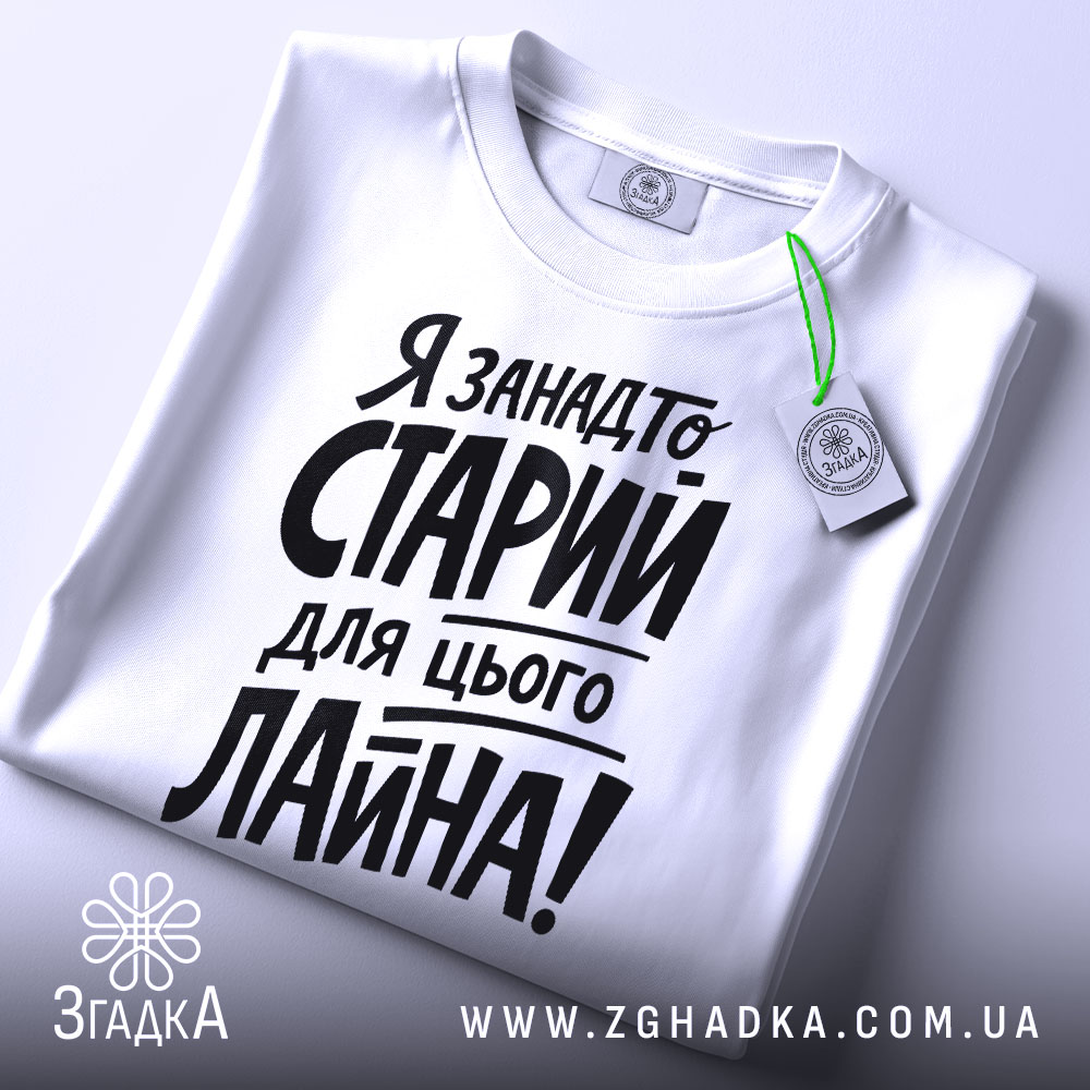 Футболка я занадто старий. Біла футболка, складена на поверхні, з видимим ярликом. Фон світлий, з легким градієнтом. Принт чорного кольору, розташований по центру, з великими літерами.