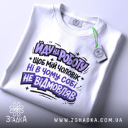 Футболка йду на роботу, біла, зображена зверху, на столі, фон світлий, принт чорного та фіолетового кольорів з текстом на українській мові, з етикеткою.